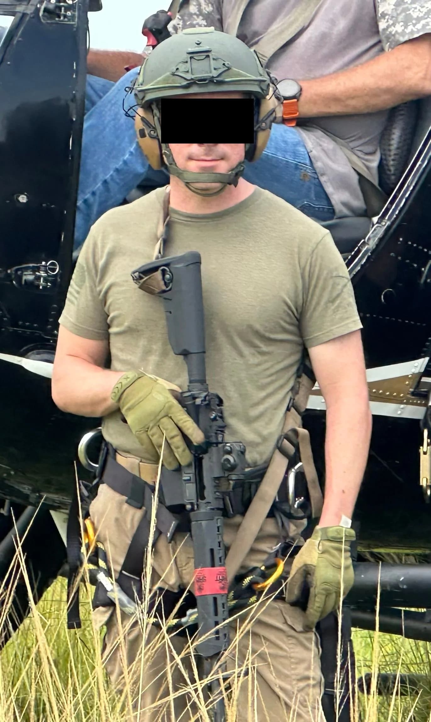 A helmeted academy candidate standing post beside the helicopter with a carbine